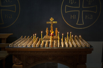 Lighted candles on a stand with golden crusifix in Russian Orthodox Christian cathedral