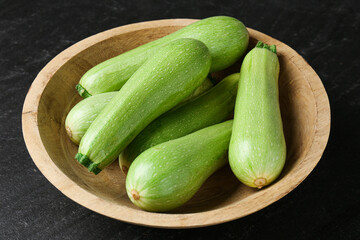 Fresh zucchinis in bowl on dark table, closeup