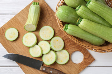 Fresh zucchinis and knife on white wooden table, flat lay