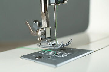 Sewing machine with green thread on grey background, closeup