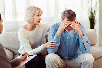 Loving Mature Wife Supporting Her Depressed Husband During Psychotherapy Session With Counselor, Free Space - Powered by Adobe