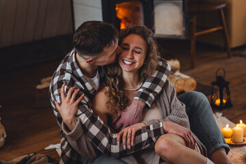 Fototapeta premium Concept of happy family relationships between man and woman. Young couple relaxed near fireplace in a cottage countryside house. Cozy atmosphere, calm lazy weekend, slow living , simple pleasures