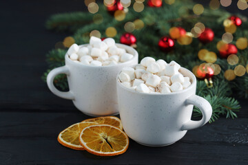 Tasty hot cocoa drinks with marshmallows in cups and dry orange slices on black wooden table, closeup