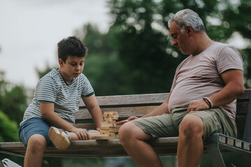 Obraz premium A father and son enjoy a bonding moment in the park, playing with building blocks on a bench. The scene captures family time, outdoor play, and creativity.