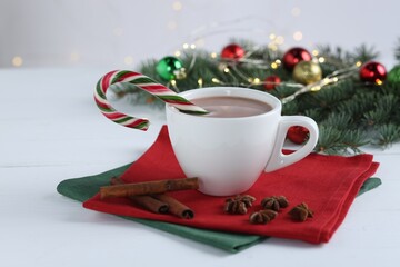 Yummy cocoa and candy cane in cup, spices and Christmas wreath on white wooden table