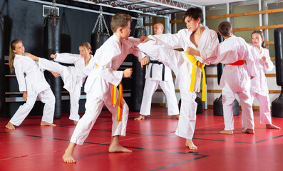 Preteen children practicing in pair karate movements with male trainer supervision