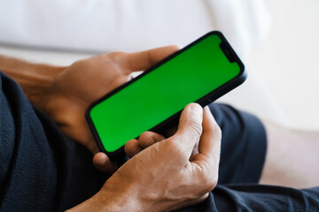 A close-up of a hand holding a smartphone with a green screen, ideal for mockups or design insertions