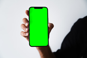 A close-up of a hand holding a smartphone with a green screen, ideal for mockups or design insertions
