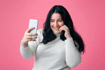 Naklejka premium Selfie Time. Pretty Plump Girl Taking Self-Portrait On Smartphone, Isolated On Pink Background, Empty Space