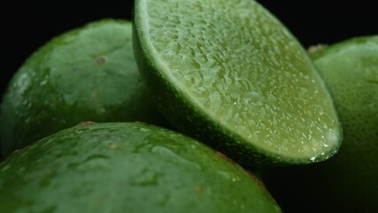 Slices of lime are meticulously arranged in a pile, set against a black background. Each lime slice is captured in stunning detail, its vibrant green hue and enticing texture. Close up. Comestible.