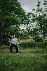 A woman stands confidently in a lush green forest park, enjoying the serene and natural surroundings. She appears relaxed and content in the peaceful outdoor setting.