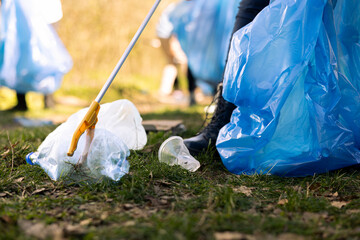 Volunteer clearing the woodland of trash and plastic waste with a long claw tool and bags, collecting rubbish. Young activist doing voluntary work to preserve forest ecosystem.