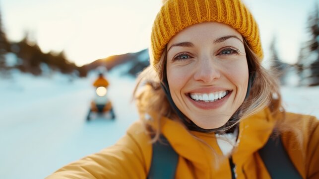 A young woman, clad in a yellow jacket and beanie, beams happily while her snowmobile speeds through a wintry landscape at sunset, exuding pure thrill.