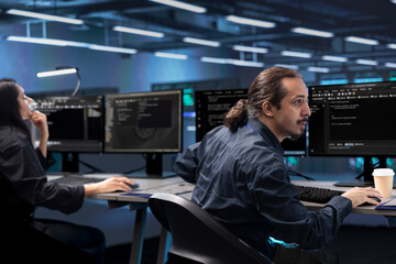 Colleagues in data center facility running system diagnostic tests on computers. IT experts at PC desk in server farm deploying error checking utilities to mend network issues