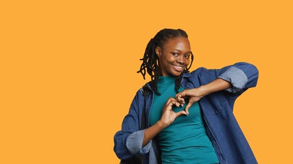 Portrait of friendly smiling african american woman doing heart symbol shape gesture with hands, being affectionate. Cheerful nurturing person showing love gesturing, studio background, camera A