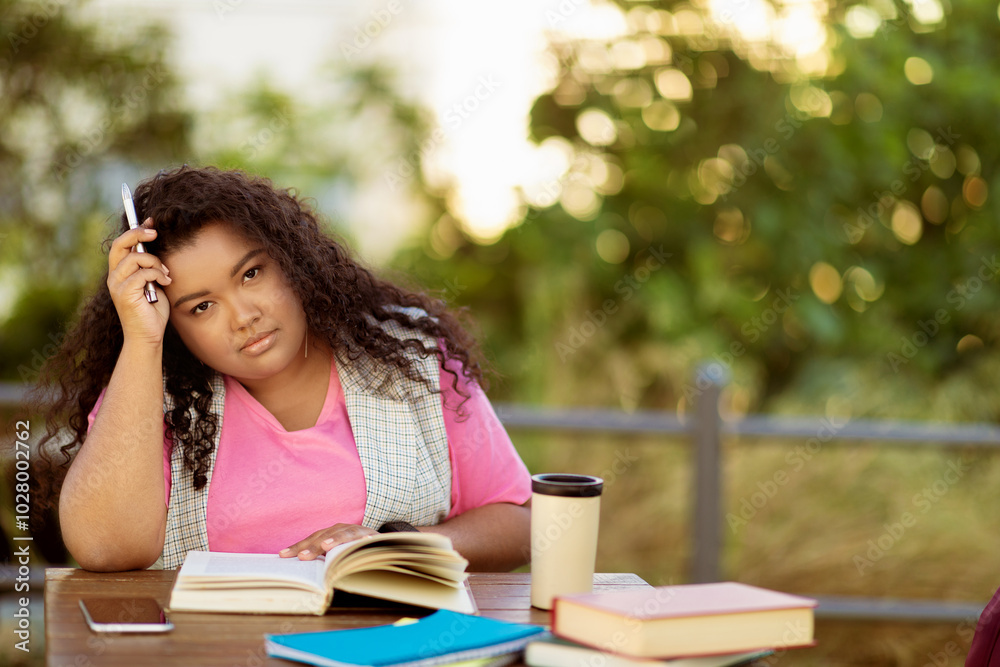 Poster a student sits at a table surrounded by books, looking thoughtfully while holding a pen. she is outd