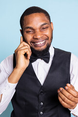 African american doorman gives information about hotel facilities on phone call, explaining all available facilities upon room reservation. Bellboy assisting future guests on telephone.