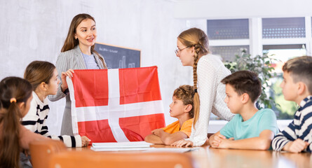 Obraz premium Decent teacher showing Denmark flag to group of preteen schoolchildren in classroom during lesson