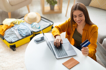 Happy young woman with credit card booking vacation at travel agency or making hotel reservation...