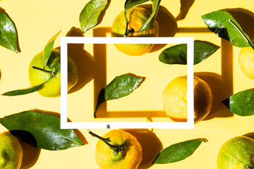Mandarins and green leaves on a yellow background with a white frame. Mockup for advertising and presentation. Top view. Copy space. Bright festive background.