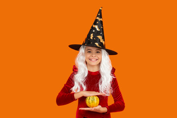 Costume party. Halloween pumpkin in hand of witch girl. Halloween witch girl isolated on orange....