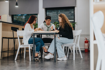 Three students work together at a table in a contemporary school environment, showcasing teamwork and collaboration.