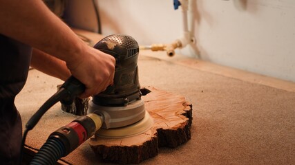 Carpenter using angle grinder on timber block to smooth surfaces with sandpaper. Woodworking professional using orbital sander equipment for furniture assembling job in studio, close up, camera A
