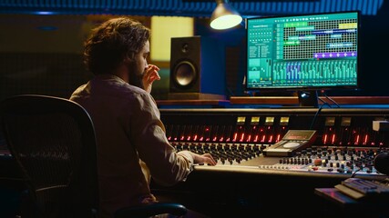 Audio technician uses mixing and mastering techniques in studio to edit and process tracks, working...