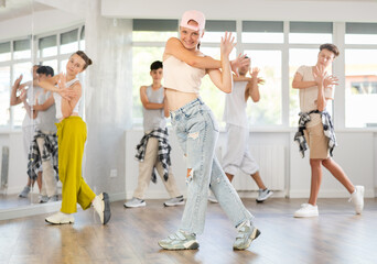 During rehearsal workout teen girl in baseball cap dances hip hop with friends. Team of dancers performs sequence of steps in combination with hand movements, energetic hobby leisure activity of youth