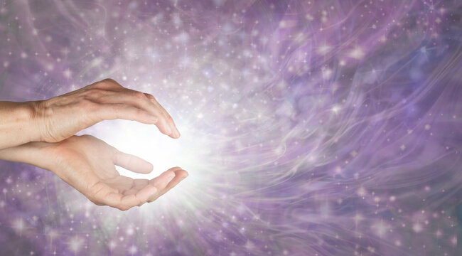 Come and enjoy some Reiki  healing energy - female cupped hands with white light and a beautiful radiating purple energy field of sparkles with copy space for a spiritual message
