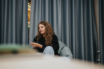 A young student with curly hair enjoys a conversation in a relaxed school setting. Her thoughtful...