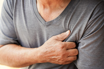 person in gray shirt is clutching their chest, possibly indicating discomfort or pain. image suggests health concern, such as heart issues or stress