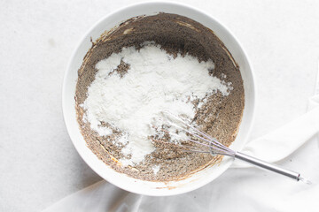 Overhead view of flour being mixed into molasses cookie dough, top view of gingerbread cookie dough in a white mixing bowl, process of making christmas cookies