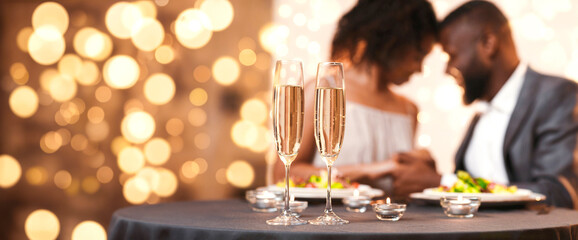 Glasses of champagne and candles on restaurant table, afro couple having romantic date