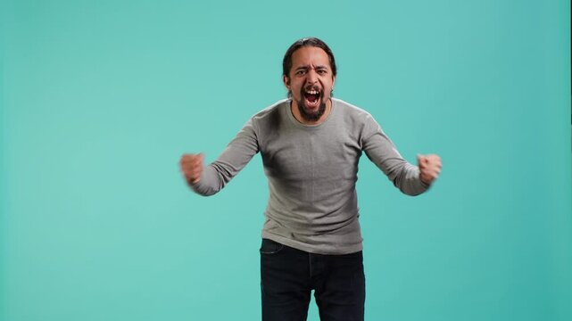 Portrait of irate man feeling outraged, yelling at friend, releasing pent up emotion, studio backdrop. Furious person full of rage screaming at mate isolated over blue studio background, camera A