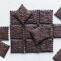 Overhead view of stamped dark molasses cookies on a parchment lined baking tray, top view of embossed gingerbread cookies on a white background