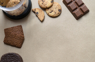 Tarro de galletas con chips de chocolate, barra de chocolate, chocolinas y alfajor sobre papel kraft. Plano desde arriba. 