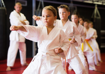 Karate kids in kimono performing kata moves with their teacher in gym during group training.