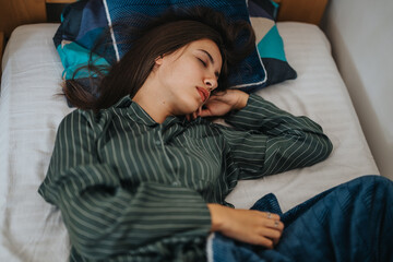 A peaceful young woman sleeps soundly in a bed, wearing comfortable striped pajamas. She is resting...