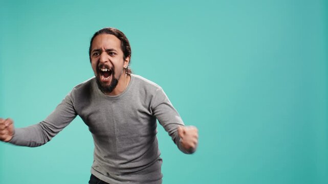 Portrait of irate man feeling outraged, yelling at friend, releasing pent up emotion, studio backdrop. Furious person full of rage screaming at mate isolated over blue studio background, camera B