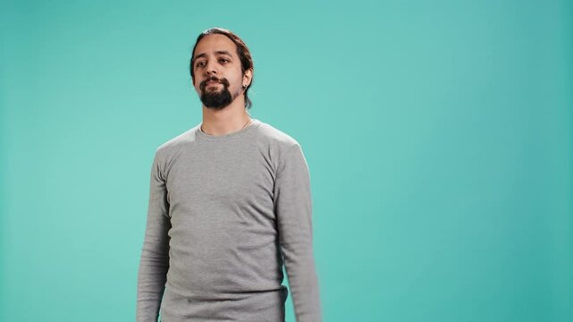 Upset man showing thumbs down sign gesturing, being disapproving. Disappointed Arab person against gaming, doing rejection hand gesture, isolated over studio background, camera B