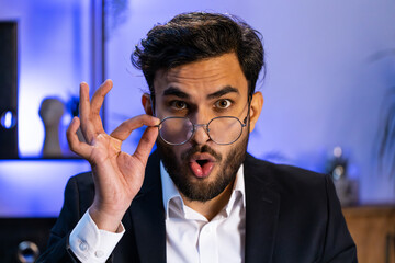 Oh my God, Wow. Indian businessman working at home office workplace, looking at camera shocked by sudden victory, game winning, lottery goal achievement, good news. Professional manager freelancer man