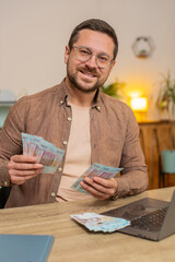 Planning budget. Rich happy businessman counting money Ukrainian hryvnias UAH cash using laptop...