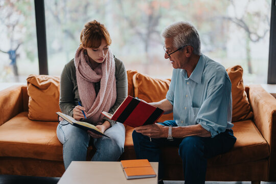 An engaged student and experienced mentor discuss study material. They sit on a comfortable orange sofa in a bright room, promoting a collaborative and relaxed learning environment.