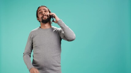 Joyous man catching up with friends in phone call using cellphone, studio background. Portrait of radiant person having conversation with mates during telephone call, camera B