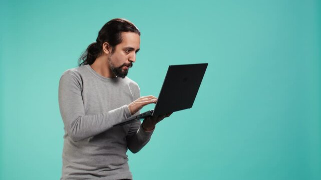 Upset man frowns while looking at laptop, dissatisfied with company profits, studio backdrop. Irked worker flabbergasted by low business income revenue, doing financial analysis on notebook, camera B