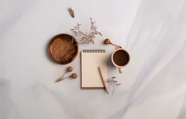 Fototapeta premium A white surface with a notebook, pencil, cup of coffee, wooden dish, and dried flowers.