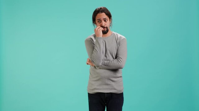 Distraught man biting nails, being afraid of receiving troubling bad news, studio background. Anxious person suffering from mental health problems, having negative emotions, camera A