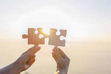 Hands trying to connect couple puzzle piece sunset sky background. Business success and strategy...