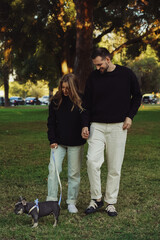 family walking with a dog in the park, french bulldog puppy walking on a leash in the park with its owner, young couple with a pet spending time outside the home